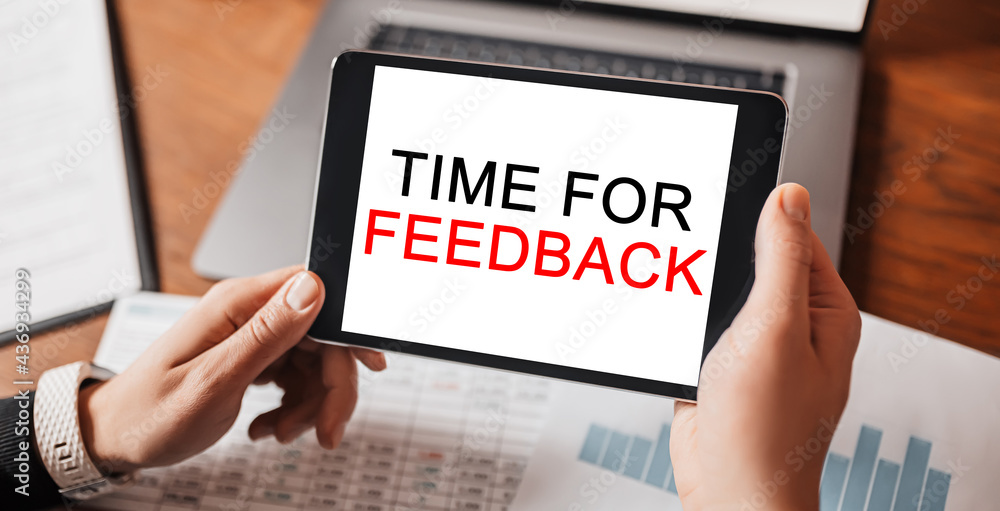 Man hands holding tablet with text Time for Feedback at workplace. Businessman working at desk with documents Man hands holding tablet with text Time for Feedback at workplace. Businessman working at desk with documents