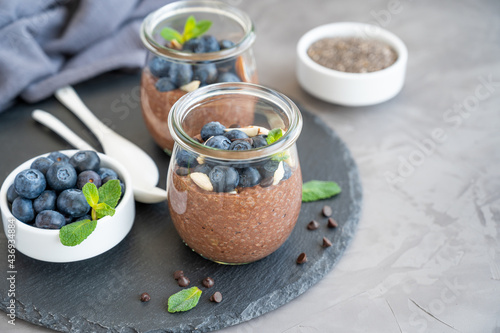 Chocolate chia pudding with blueberry, almonds and mint on top in a glass jar on a gray concrete background. Healthy food. Copy space.