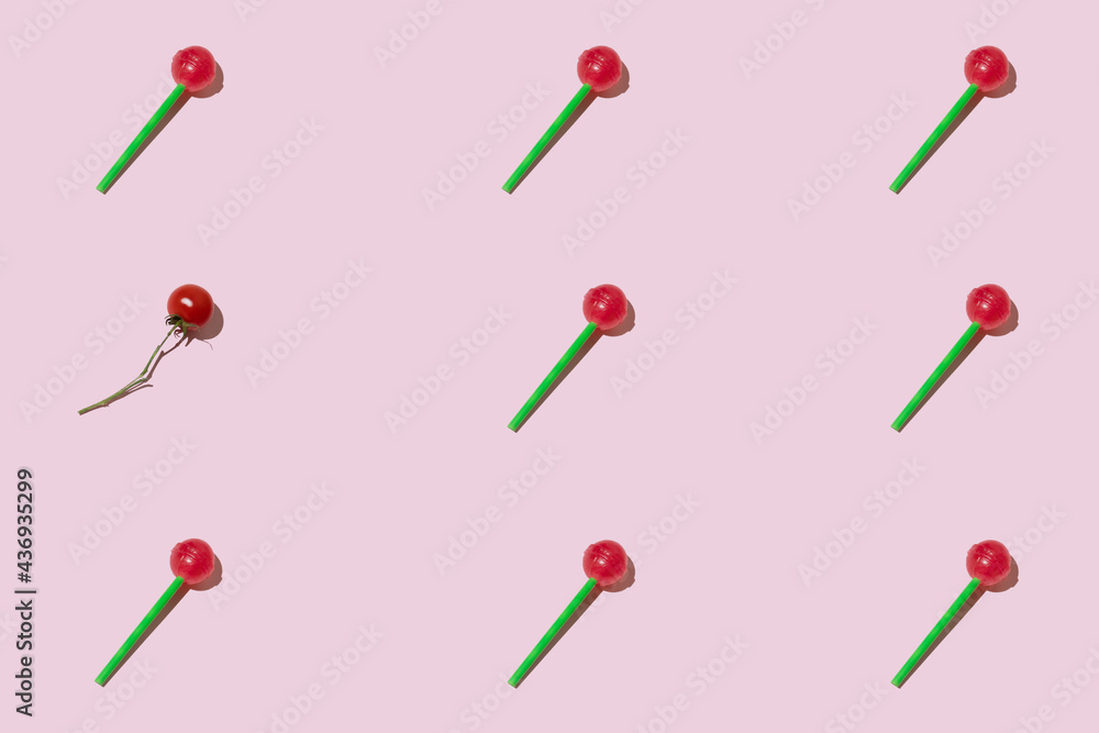 Colorful pattern made of red lollipops with green stick and one cherry tomato against pastel pink sun lit background. Minimal creative breaking pattern food concept. Colorful pattern made of red lollipops with green stick and one cherry tomato against pastel pink sun lit background. Minimal creative breaking pattern food concept.
