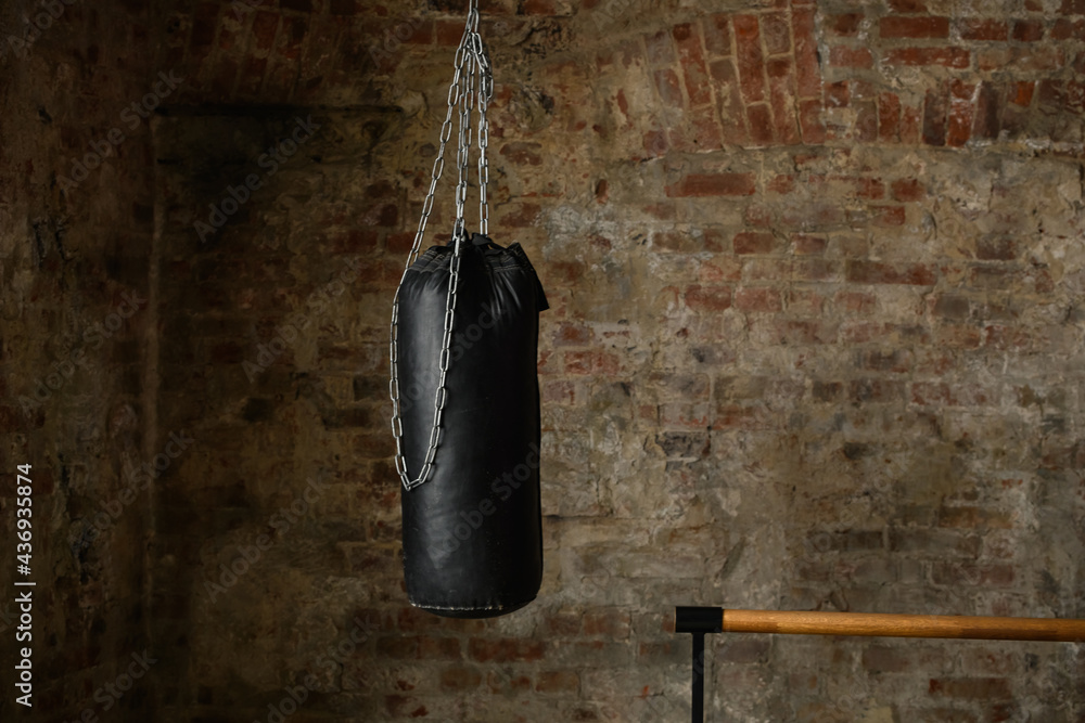 black punching bag on chains on the background of an old wall