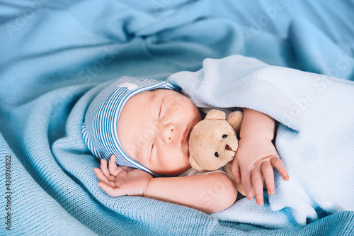 Newborn sleep at first days of life. Portrait of new born baby one week old with cute soft toy in crib in cloth background.