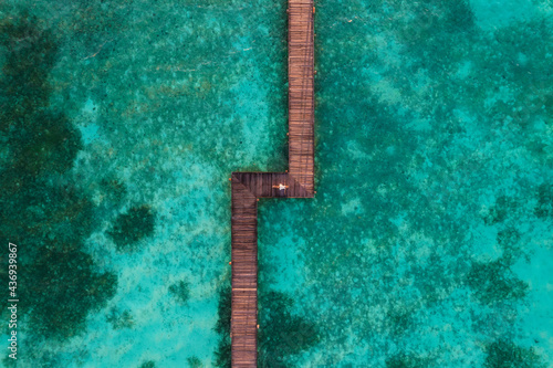 Aerial view of a woman with elegant dress laying down on a long pier near a luxury resort along the ocean, Malé, Maldives.