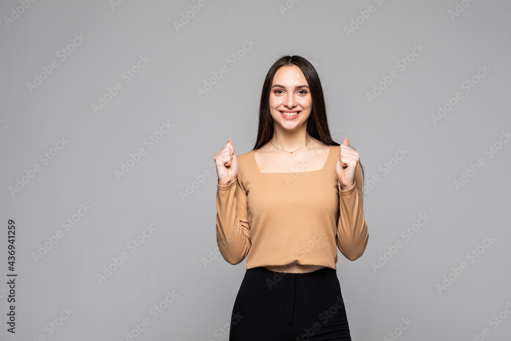 Young cheerful woman making winner gesture and smiling isolated over grey background Young cheerful woman making winner gesture and smiling isolated over grey background