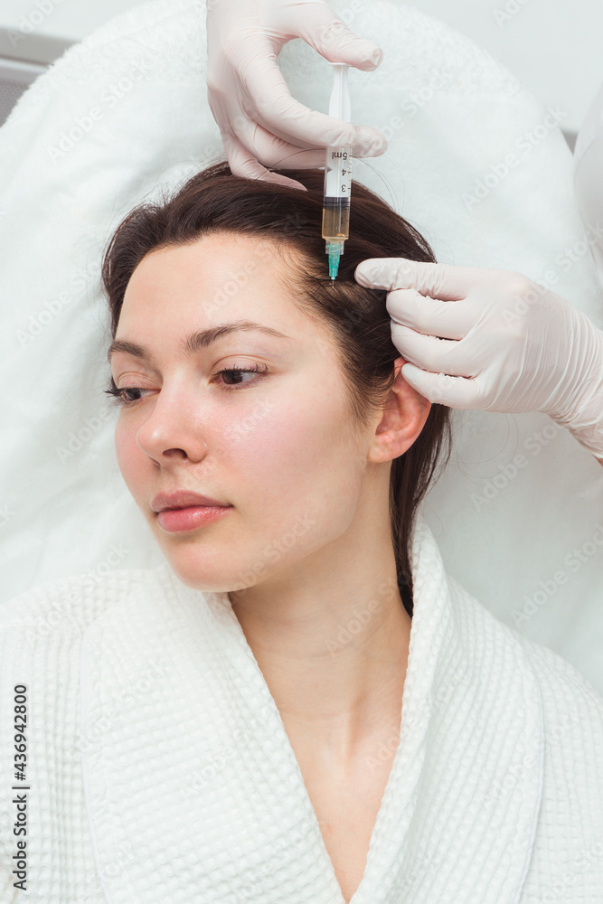 Naklejka premium A woman getting a shot in the head at a cosmetology clinic. mesotherapy for hair growth.