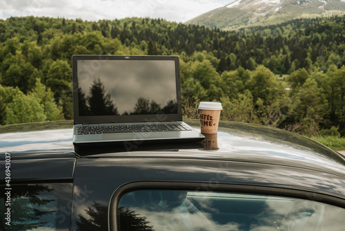 outdoors laptop with coffee cup on the car, remote location in nature with beautiful mountains internet connection, working on the road concept