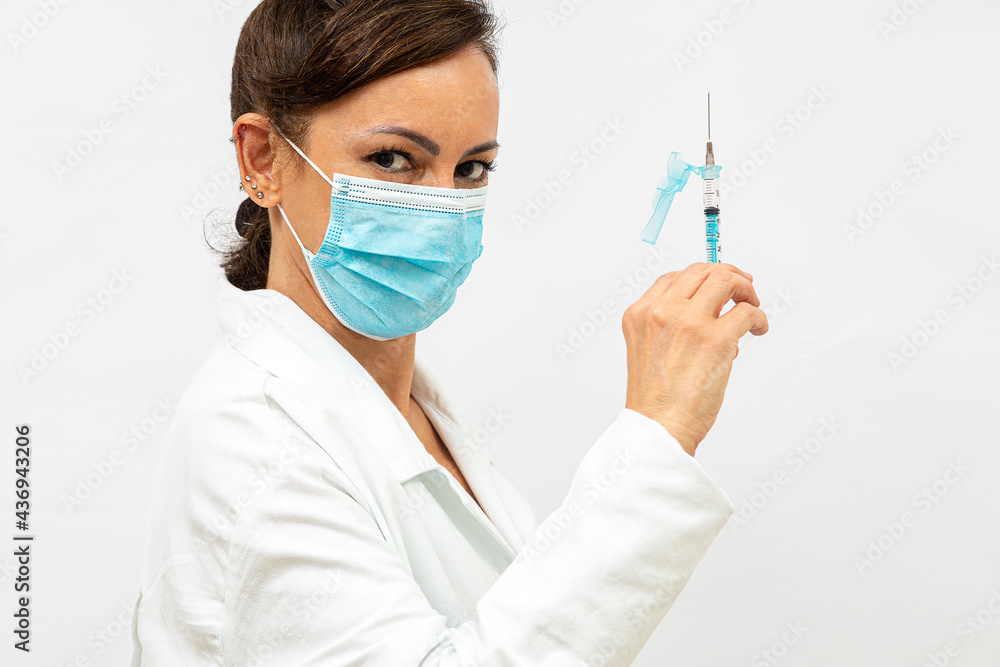 Enfermeira na máscara de perfil com um olhar convidativo, mostrando e apontando a seringa para cima, no fundo branco Enfermeira na máscara de perfil com um olhar convidativo, mostrando e apontando a seringa para cima, no fundo branco