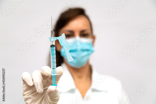 Seringa de vacina em foco nas mãos de uma médica com luvas e mascara cirugica desfocado ao fundo photo