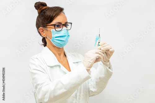 Médica de óculos, usando máscara protetora, segurando uma seringa com as duas mãos usando luvas cirúrgicas. photo
