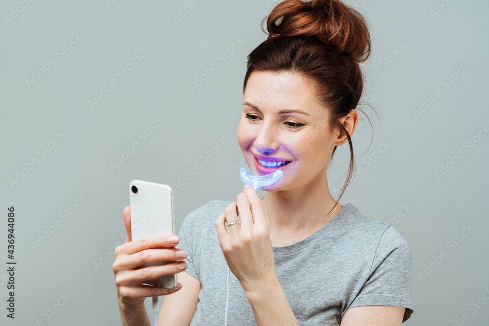 A young woman is engaged in home teeth whitening. Complex for teeth whitening with UV lamp A young woman is engaged in home teeth whitening. Complex for teeth whitening with UV lamp