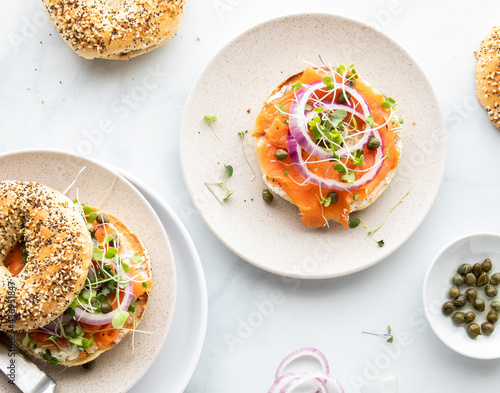 Top down view of a bagel topped with salmon lox and garnished with red onion, sprouts and capers.