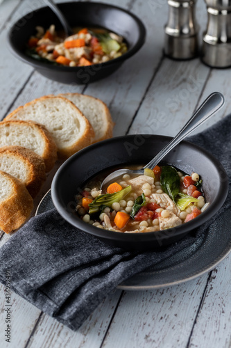 Vertical view of chicken and couscous soup in black bowls, served with bread.