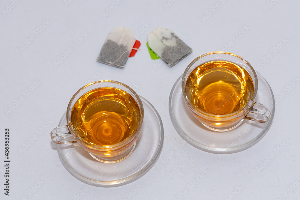 Two cups of black leaf tea with tea bags kept alongside with white background 