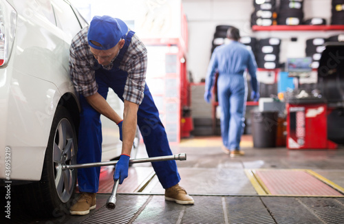 Mechanic engaged in replacement of tyre on car wheel in auto workshop