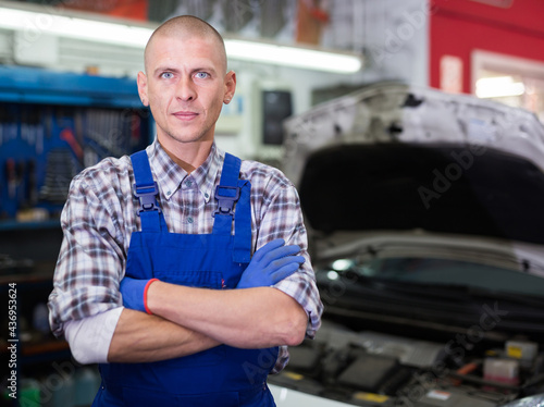 Confident auto mechanic man standing with crossed arms in auto workshop