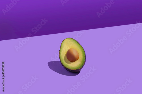 Half an avocado with stone. Pop style. Background of violet colors of different shades.