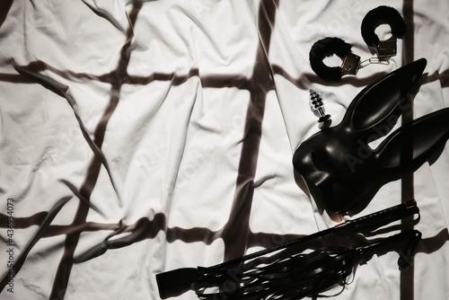 set of sex toys on the background of a white sheet in bed. Leather whip, handcuffs and mask