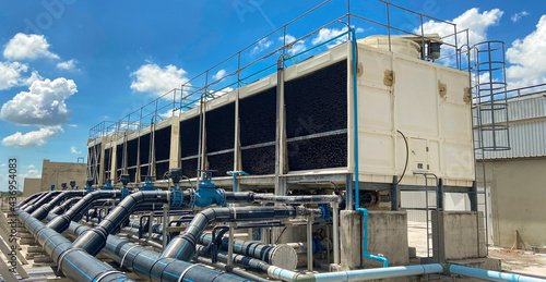 The cooling tower is located in a large data center building installed on the roof on a bright blue sky. And there are white clouds - pictures