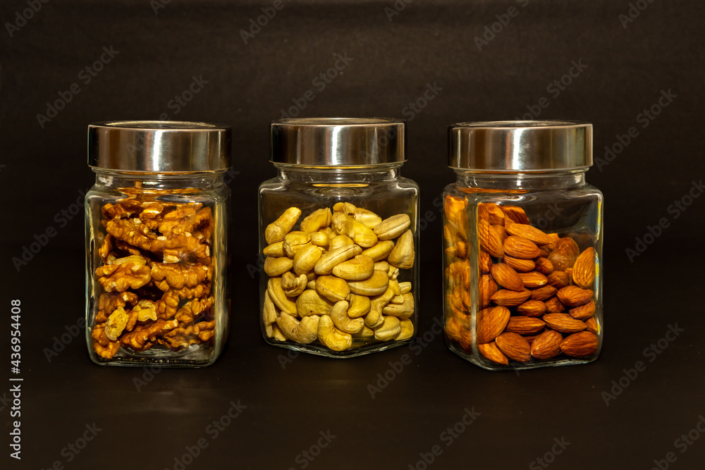 Glass jars filled with walnuts, cashew nuts and almonds displayed with black background Glass jars filled with walnuts, cashew nuts and almonds displayed with black background