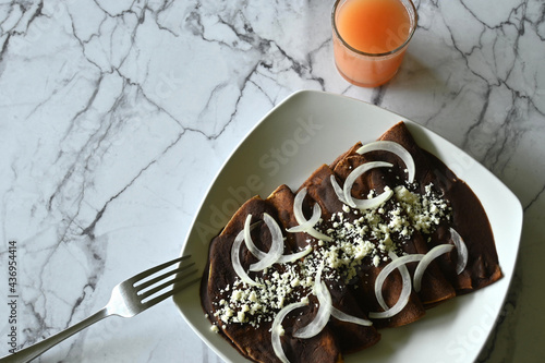 Overhead shot of enfrijoladas with onion and cheese, glass of grapefruit juice, fork, with marble background, with copy space photo