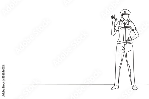 Single one line drawing of female pilot stands with gesture okay and complete uniform serves airplane passengers fly to destination. Modern continuous line draw design graphic vector illustration