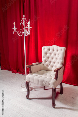 White luxury chair, vintage candles next to it, and it's all on a red background
