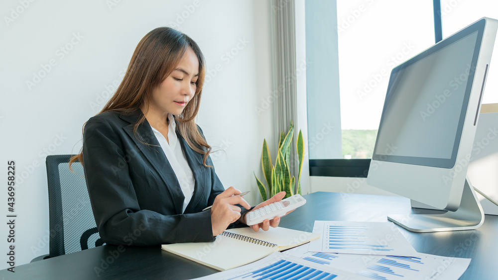 A confident young businessman analyzes graph data and calculates with a calculator and uses a computer while in the office. A confident young businessman analyzes graph data and calculates with a calculator and uses a computer while in the office.