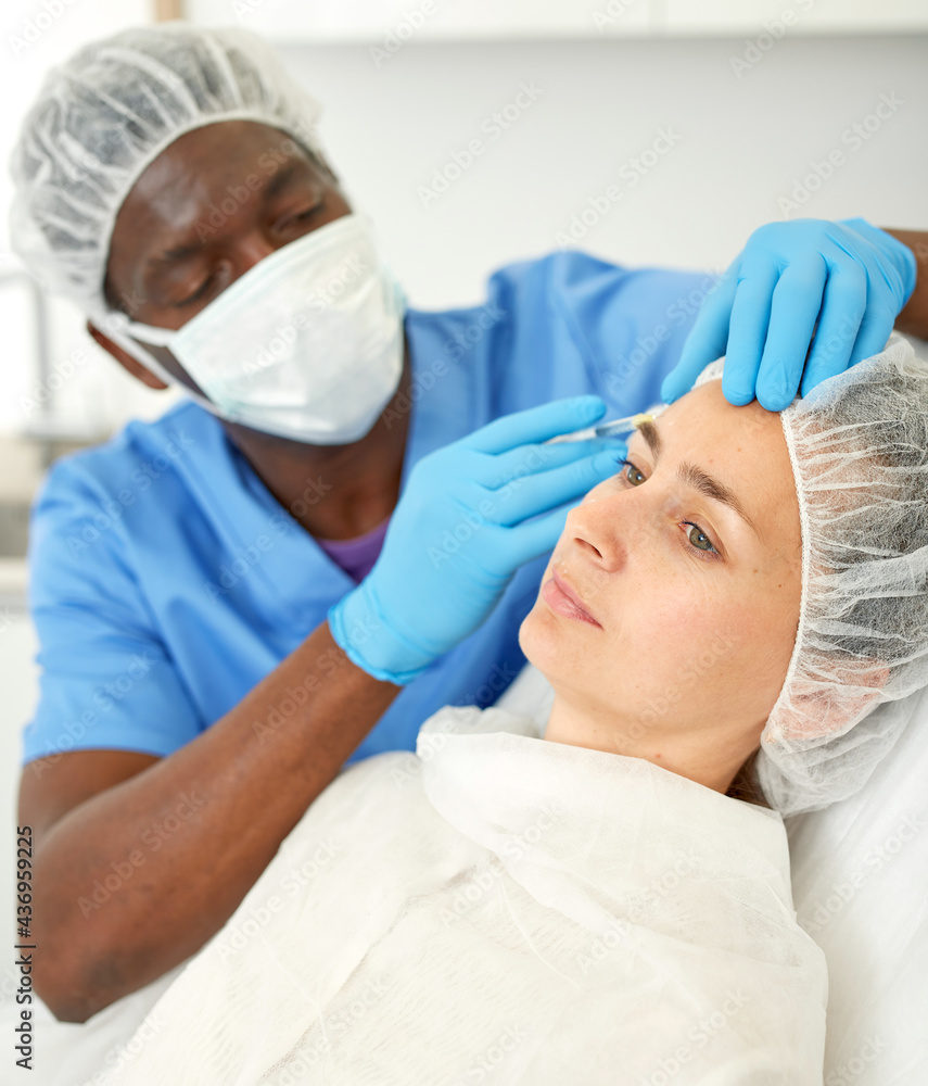 Naklejka premium Male doctor in mask is doing injection to woman patient in skin of face in estetic clinic