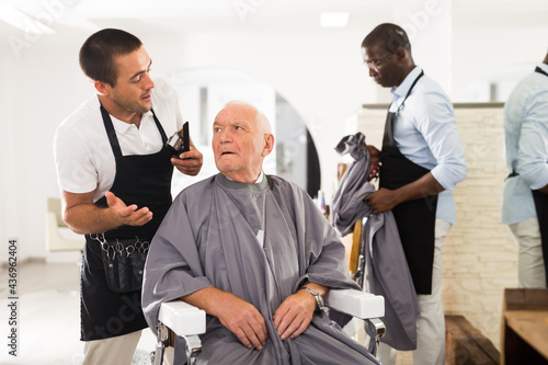 Aged male client expressing dissatisfaction with haircut to perplexed hairdresser at barber shop