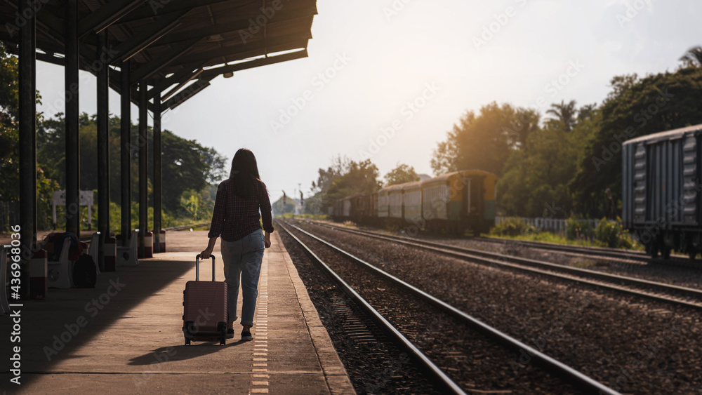 A female tourist holding a pink bag is waiting for a train at the train station.
