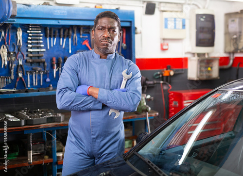 Professional man car mechanician standing near repairable car in auto repair shop