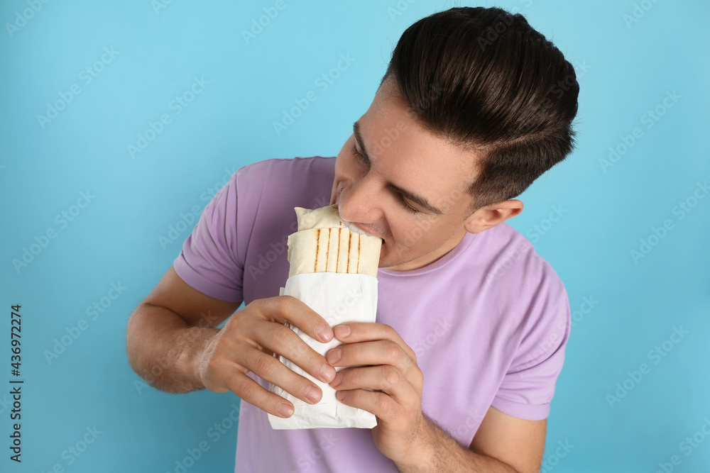 Man eating delicious shawarma on turquoise background Man eating delicious shawarma on turquoise background