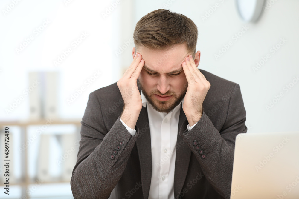 Young man suffering from migraine in office Young man suffering from migraine in office