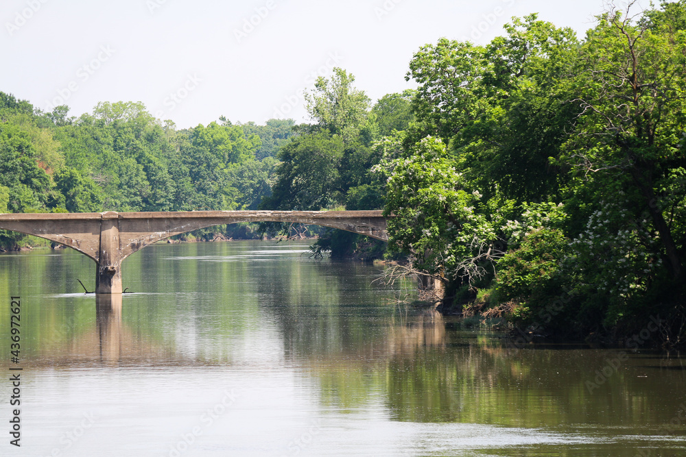 Fototapeta premium old abandoned concrete arch roadway or train railway bridge over a calm river with trees and clear sky