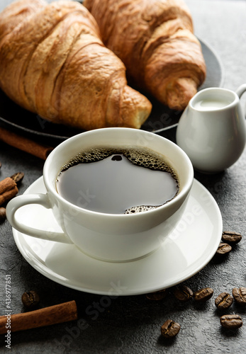 Close-up coffee cup with croissants and coffee beans.