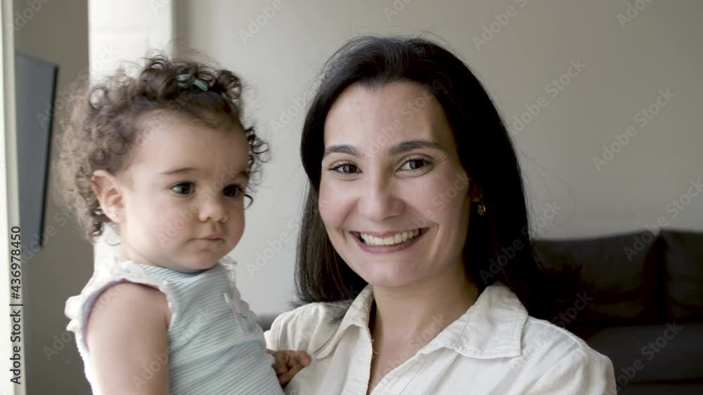 Front view of mom and infant looking at camera and smiling. Caucasian mother holding her serious baby and posing. Family, togetherness concept. Front view of mom and infant looking at camera and smiling. Caucasian mother holding her serious baby and posing. Family, togetherness concept.