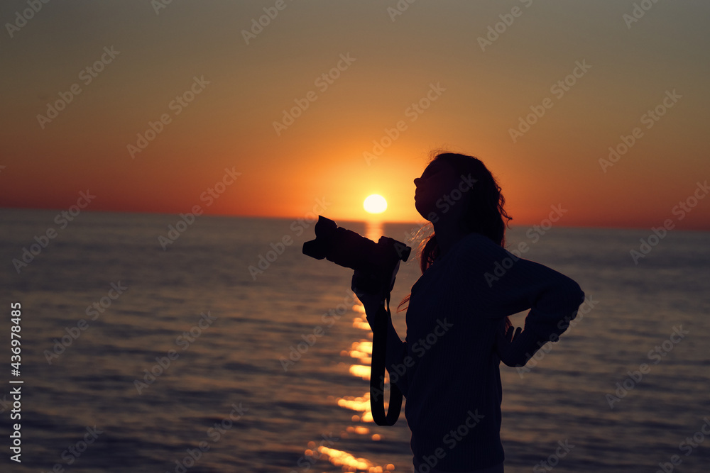 silhouette of a woman with a camera at sunset near the sea beach landscape