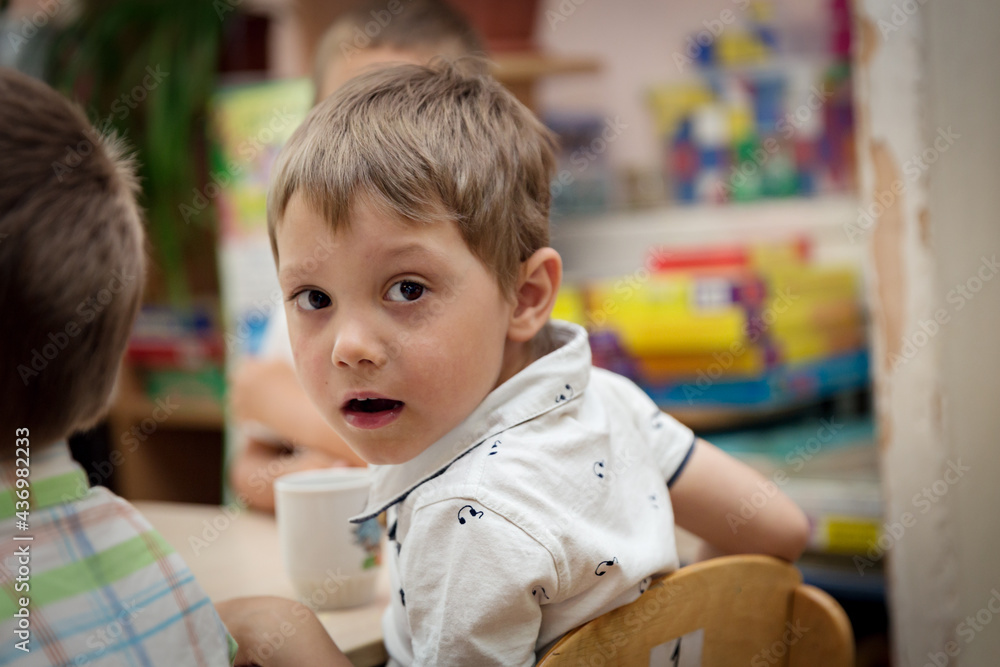 cute caucasian boy sitting at the table in kindergarden having breackfast. Image with selective focus cute caucasian boy sitting at the table in kindergarden having breackfast. Image with selective focus