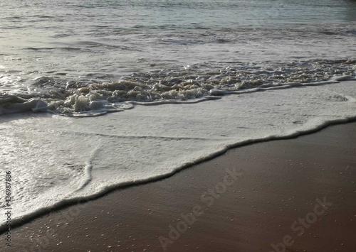 Waves hit the sandy beach in the evening before sunset.
