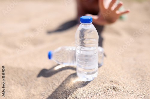 Man reaches for bottle of water standing on sand