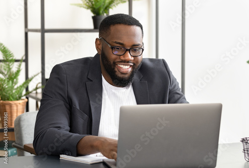 Portrait of happy African American male business with laptop sitting in the office. Successful freelancer working with laptop while sitting at workplacere