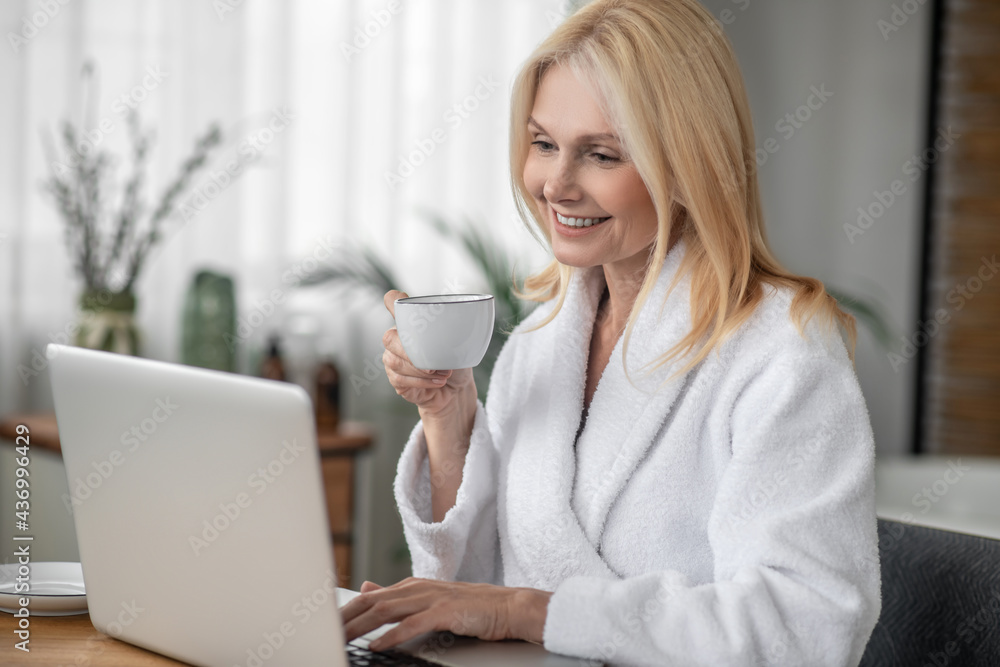 Smiling long-haired woman having coffee and watching something online Smiling long-haired woman having coffee and watching something online