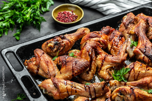 Baked chicken wings and legs on baking tray. Wings of barbecue on dark stone table. Top view, Food recipe background. Close up