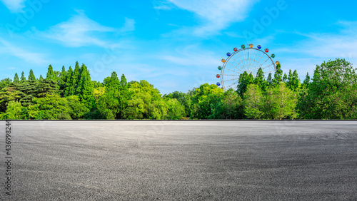 Asphalt road ground and ferris wheel with green forest scenery.