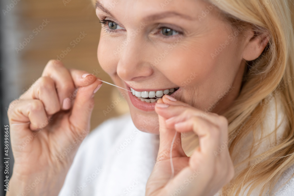 A good-looking smiling woman cleaning her teeth with a dental floss A good-looking smiling woman cleaning her teeth with a dental floss