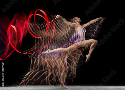 Young graceful girl rhythmic gymnast in motion isolated in mixed light on dark background. photo