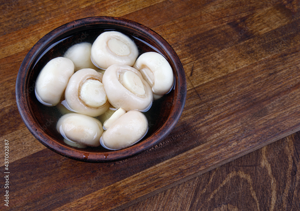 A plate with pickled champignons on a wooden board. A plate with pickled champignons on a wooden board.