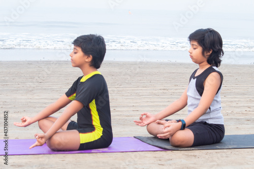 Two boys meditating in yoga lotus position at beach