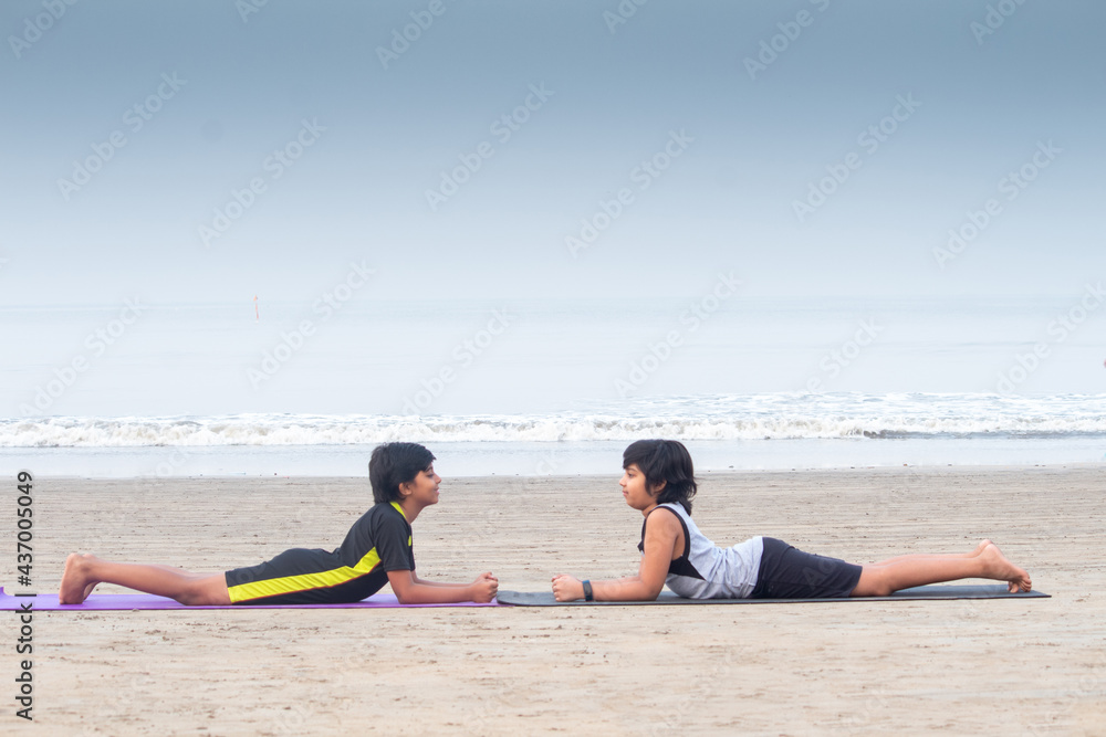 Profile of two boys practicing yoga cobra pose face to face on exercise mat at beach