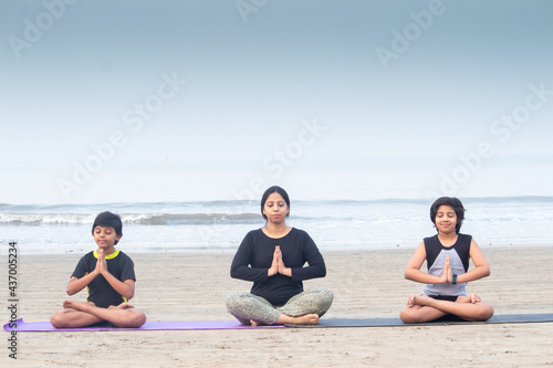 Mother with her two sons practicing yoga at beach