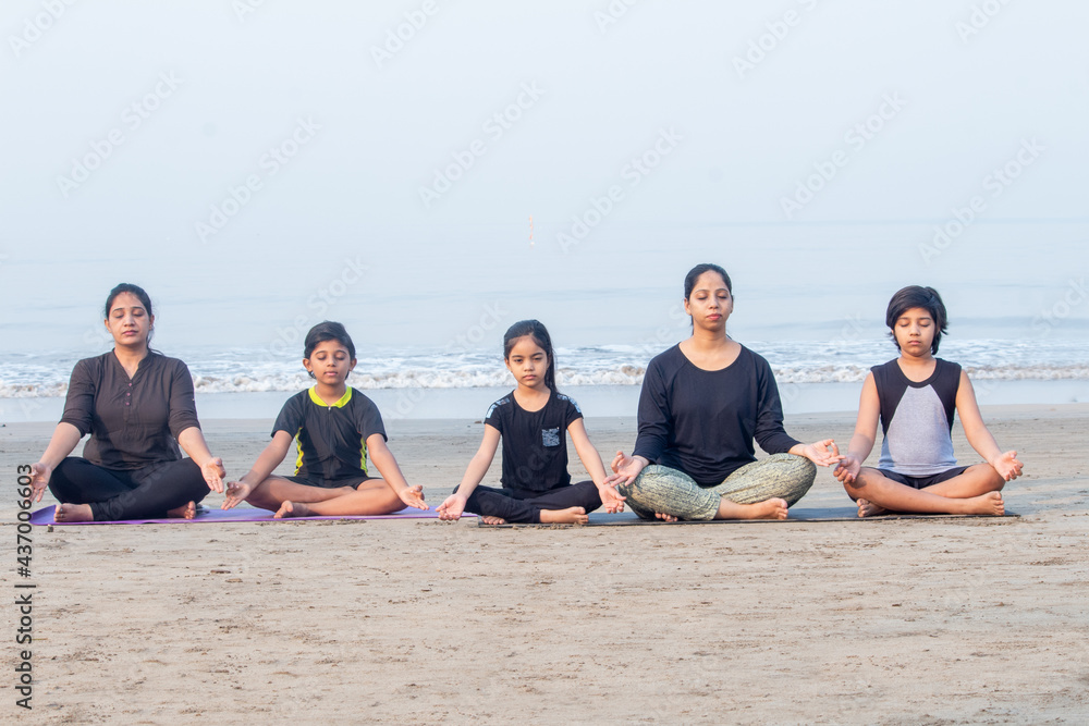 Two women with boys and little girl meditating in lotus position at beach Two women with boys and little girl meditating in lotus position at beach